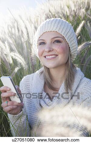 Stock Image - Young woman texting on smartphone in long grass. Fotosearch