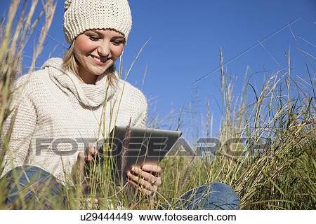 Young woman using digital tablet in long grass View Large Photo Image Stock Photo - Young woman using digital tablet in long grass. Fotosearch