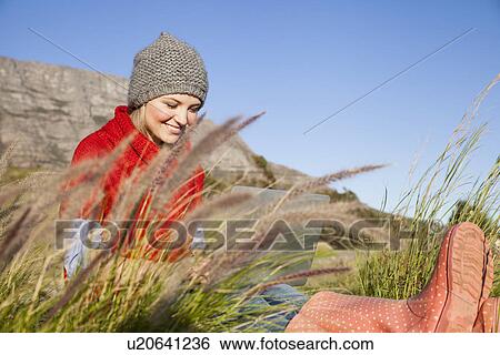 Stock Photograph - Young woman using laptop in grassy field. Fotosearch