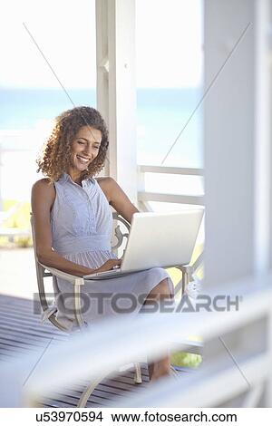 Young woman using laptop on beach house balcony View Large Photo Image Picture - Young woman using laptop on beach house balcony. Fotosearch