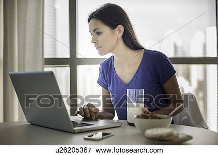 Stock Photo - Young woman using laptop whilst having breakfast. Fotosearch