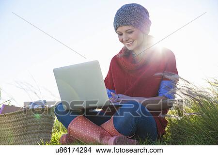 Young woman using laptop whilst sitting in long grass View Large Photo Image Picture - Young woman using laptop whilst sitting in long grass. Fotosearch