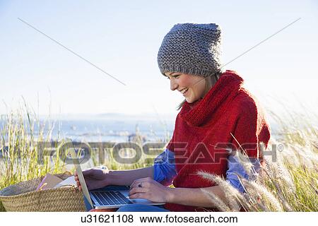 Stock Photo - Young woman using laptop whilst sitting on hilltop. Fotosearch