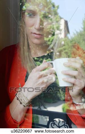 Young woman with coffee cup gazing out of window View Large Photo Image Stock Photo - Young woman with coffee cup gazing out of window. Fotosearch