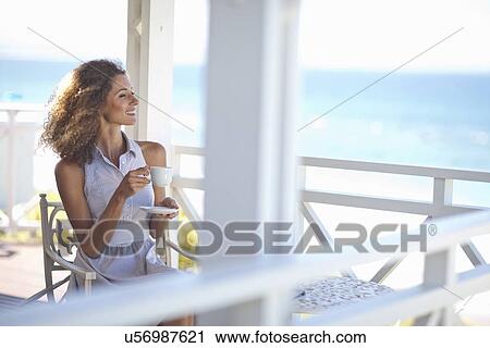 Young woman with coffee gazing out to sea from beach house balcony View Large Photo Image Stock Image - Young woman with coffee gazing out to sea from beach house balcony. Fotosearch