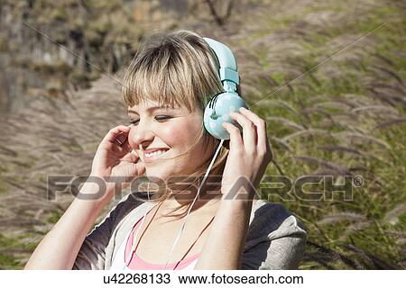 Young woman with eyes closed listening to headphones in long grass View Large Photo Image Stock Image - Young woman with eyes closed listening to headphones in long grass. Fotosearch