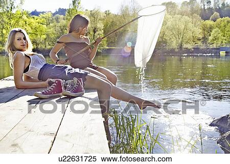 Young women sitting on jetty, one holding fishing net View Large Photo Image Stock Photography - Young women sitting on jetty, one holding fishing net. Fotosearch