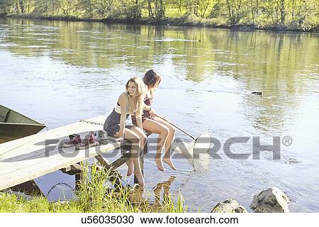 Stock Image - Young women sitting on jetty. Fotosearch