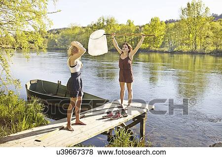 Young women standing on jetty, one holding fishing net View Large Photo Image Stock Photo - Young women standing on jetty, one holding fishing net. Fotosearch