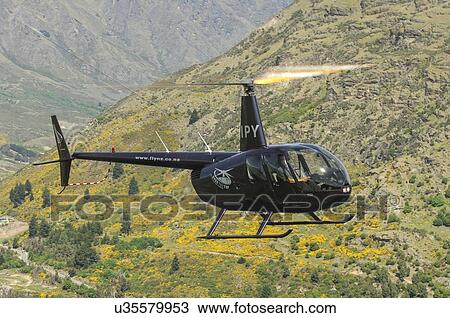 Stock Image - Robinson R44 helicopter in flight near Queenstown. Fotosearch