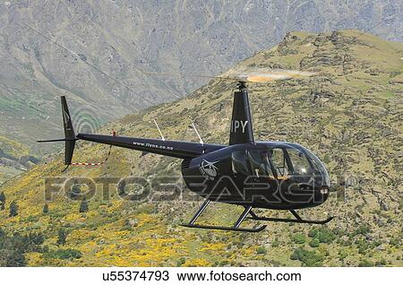 Stock Image - Robinson R44 helicopter in flight near Queenstown. Fotosearch
