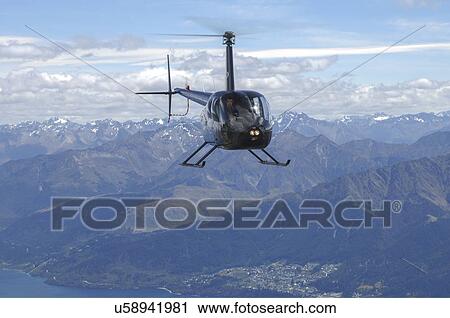 Stock Image - Robinspon R44 helicopter in flight over Lake Wakatipu and Queenstown, New Zealand. Fotosearch