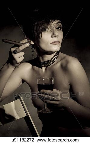 Stock Image - Black and white of topless woman drinking wine and smoking a cigar. Fotosearch