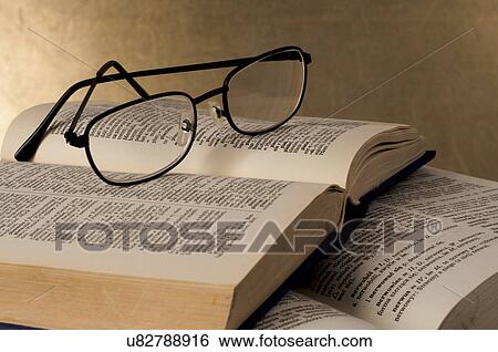 Stock Photograph - Eye glasses on pile of open books. Fotosearch