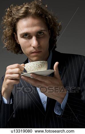 Stock Image - Young man holding coffee cup and saucer. Fotosearch