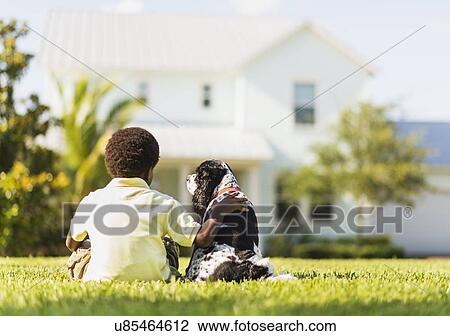Stock Image - Back view of boy (6-7) sitting with dog. Fotosearch