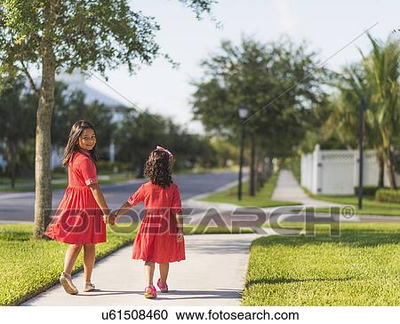 Stock Image - Back view of girls( 4-5, 8-9) holding hands. Fotosearch