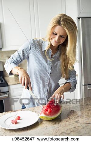 Stock Photo - Blonde housewife cutting watermelon. Fotosearch