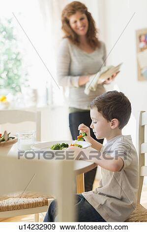 boy (6-7) eating healthy dinner, mother in background View Large Photo Image Stock Photo - boy (6-7) eating healthy dinner, mother in background. Fotosearch