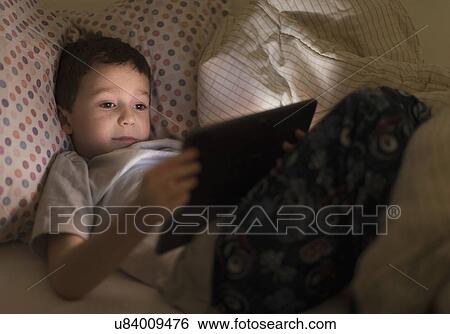 Stock Photograph - boy (6-7) using digital tablet in bed. Fotosearch