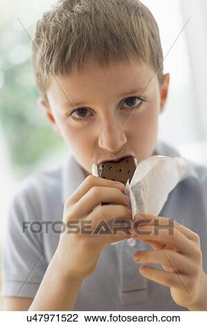Stock Image - boy (8-9) eating ice cream sandwich. Fotosearch