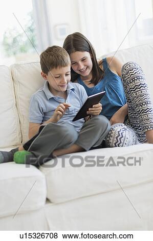 Boy and girl (8-9, 10-11) sitting on sofa using digital tablet View Large Photo Image Stock Photo - Boy and girl (8-9, 10-11) sitting on sofa using digital tablet. Fotosearch