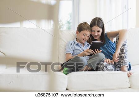 Stock Photo - Boy and girl (8-9, 10-11) sitting on sofa using digital tablet. Fotosearch