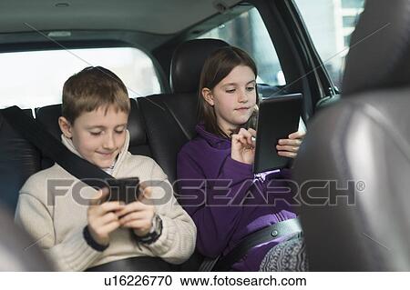 Stock Image - Boy and girl (8-9, 10-11) using digital tablet and smart phone in car. Fotosearch