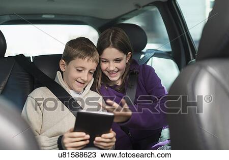 Stock Image - Boy and girl (8-9, 10-11) using digital tablet in car. Fotosearch