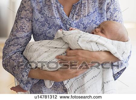 Stock Image - Close up of baby boy (2-5 months) sleeping in mother's arms. Fotosearch