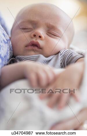 Stock Photo - Close up of baby boy (2-5 months) sleeping in mother's arms. Fotosearch