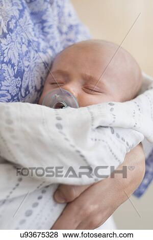 Stock Photo - Close up of baby boy (2-5 months) sleeping in mother's arms. Fotosearch