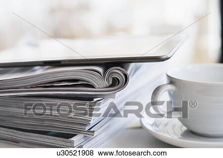 Stock Photo - Close up of coffee cup and digital tablet on top of magazine stack. Fotosearch
