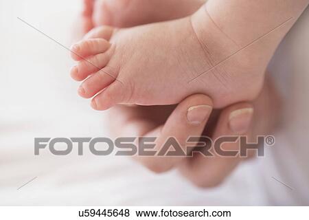 Stock Photo - Close up of mother's hand touching baby boy's(2-5 months) foot. Fotosearch
