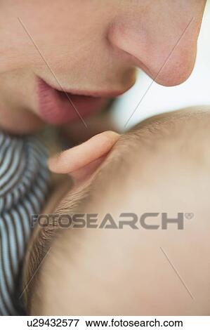 Stock Photo - Close up of mother's mouth whispering into baby boy's(2-5 months) ear. Fotosearch