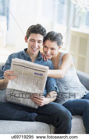 Stock Photography - Couple reading newspaper on sofa. Fotosearch
