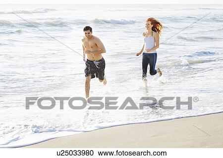Stock Image - Couple running on beach. Fotosearch