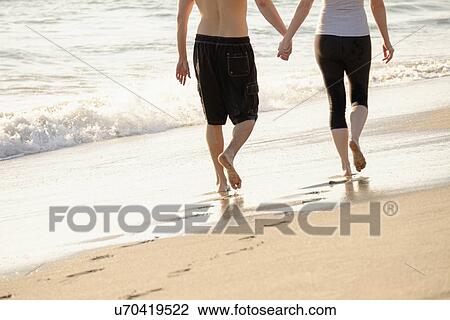 Stock Image - Couple walking on beach, low section. Fotosearch