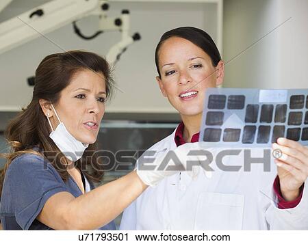 Stock Image - Dentist and assistant looking at x-ray. Fotosearch
