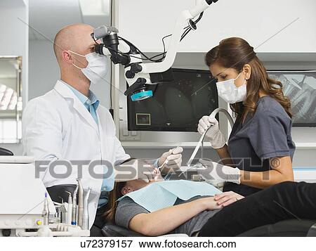 Stock Photo - Dentist operation on patient and using microscope. Fotosearch