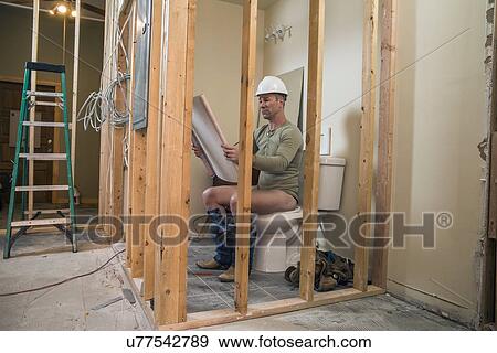 Stock Photo - Engineer examining blueprint inside new structure sitting on toilet. Fotosearch