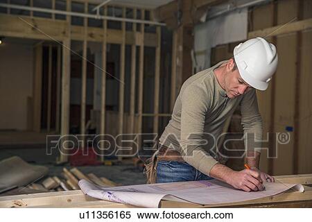 Stock Photography - Engineer examining blueprint inside new structure. Fotosearch