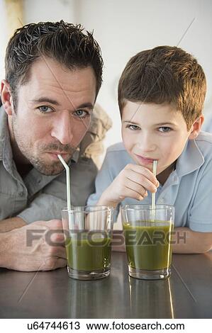 Stock Image - Father and son (8-9) drinking juice. Fotosearch