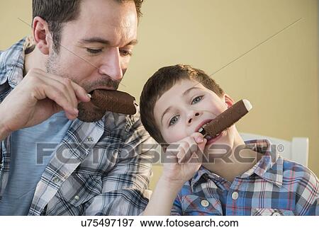 Stock Photo - Father and son (8-9) eating ice creams. Fotosearch