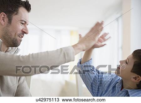 Stock Image - Father and son (8-9) high fiving . Fotosearch