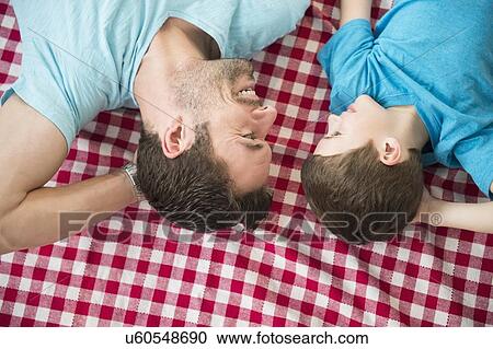 Stock Image - Father and son (8-9) relaxing on checked blanket. Fotosearch