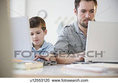 Stock Image - Father and son (8-9) working on laptops. Fotosearch