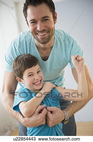 Stock Image - Father embracing son (8-9), Boy flexing muscles. Fotosearch