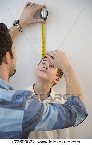 Stock Image - Father measuring height of son (8-9) . Fotosearch