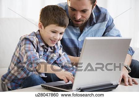 Stock Image - Father working on laptop with his son (8-9) . Fotosearch
